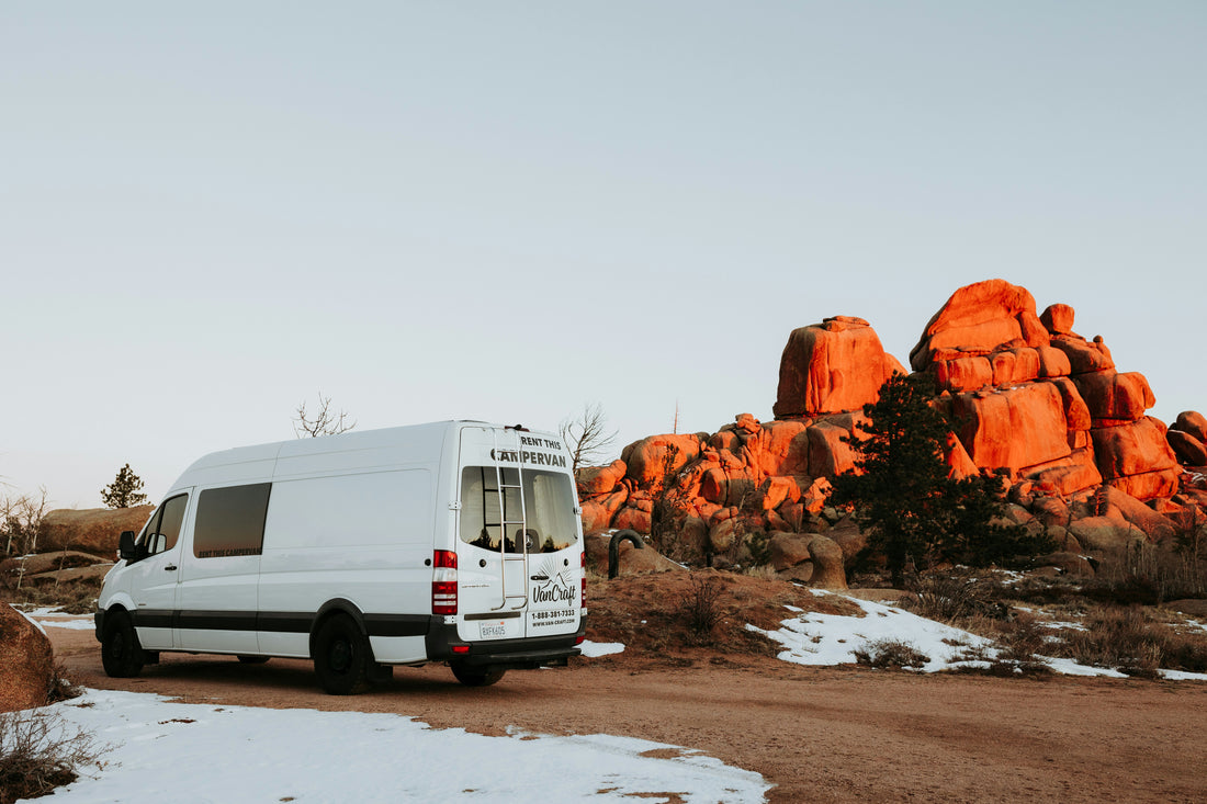 alt= White RV parked in front of rocky formation.